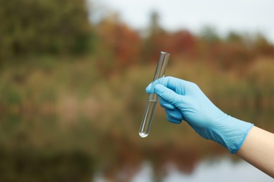 Photo of Examination of water quality. Researcher holding test tube with sample outdoors, closeup. Space for text