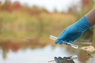 Photo of Examination of water quality. Researcher taking water sample from lake outdoors, closeup. Space for text