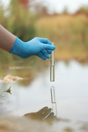 Photo of Examination of water quality. Researcher holding test tube with sample from lake outdoors, closeup