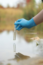 Photo of Examination of water quality. Researcher holding test tube with sample from lake outdoors, closeup