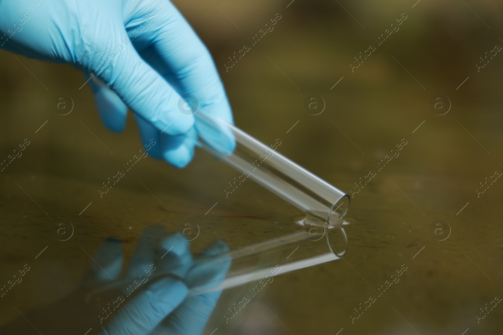 Photo of Examination of water quality. Researcher taking water sample from lake outdoors, closeup