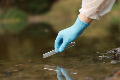 Photo of Examination of water quality. Researcher taking water sample from lake outdoors, closeup