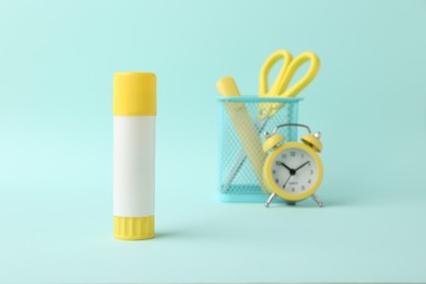 Photo of Glue stick, alarm clock, holder and scissors on turquoise background