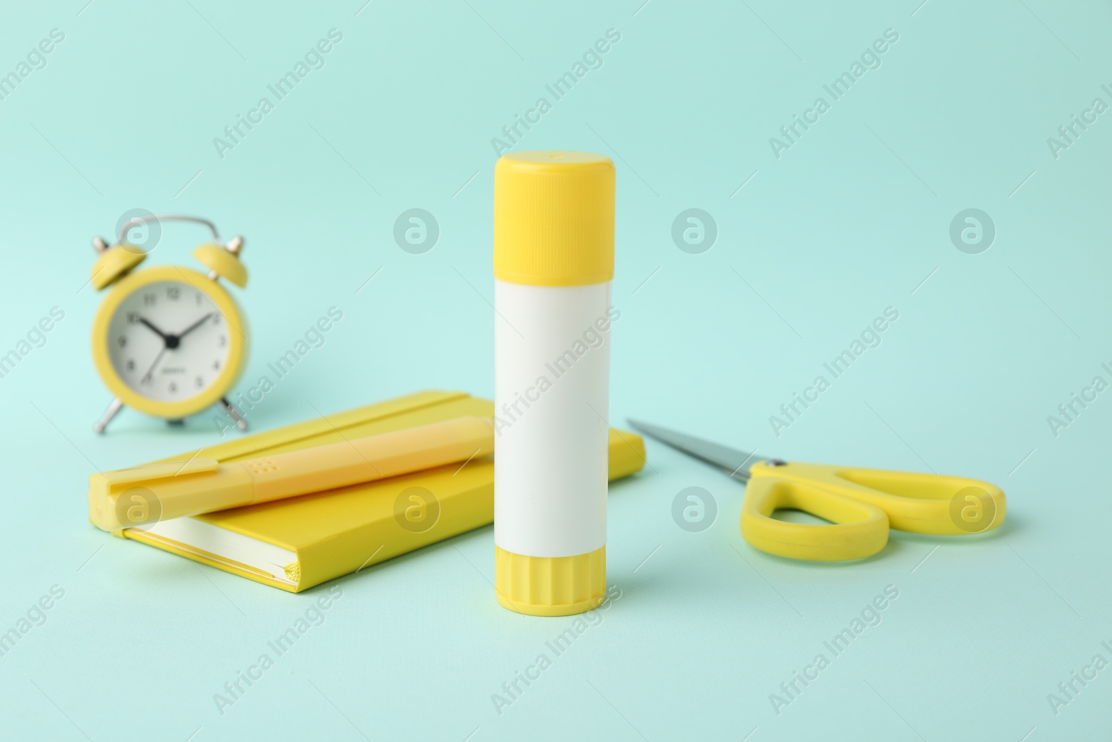 Photo of Glue stick, alarm clock, holder, scissors and notebook on turquoise background