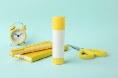 Glue stick, alarm clock, holder, scissors and notebook on turquoise background