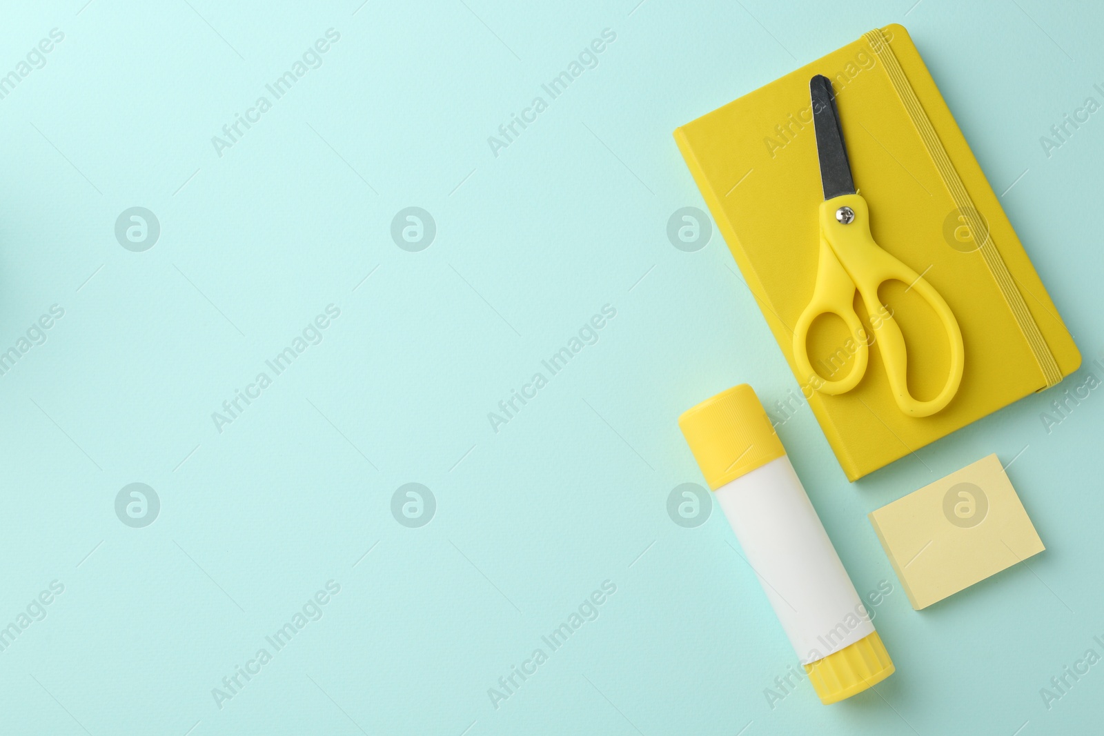 Photo of Glue stick, notebook and scissors on turquoise background, flat lay. Space for text