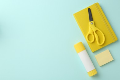 Photo of Glue stick, notebook and scissors on turquoise background, flat lay. Space for text