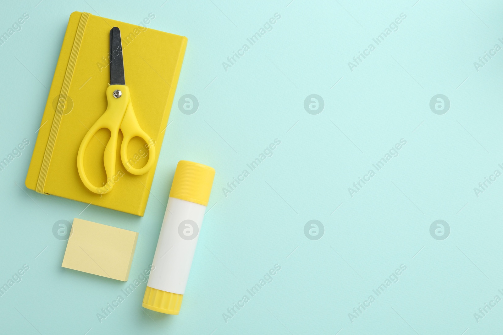 Photo of Glue stick, notebook and scissors on turquoise background, flat lay. Space for text