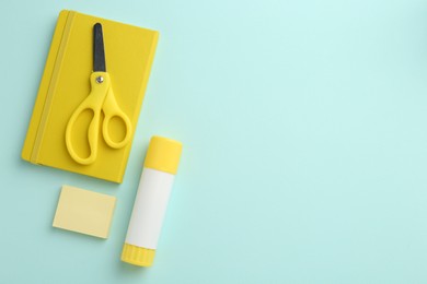 Photo of Glue stick, notebook and scissors on turquoise background, flat lay. Space for text