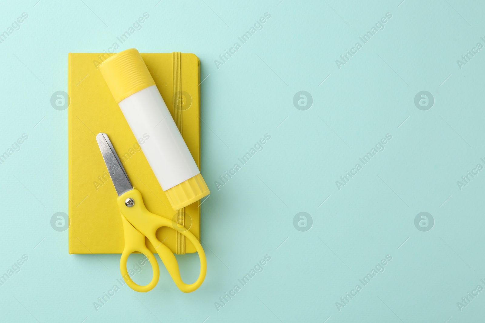 Photo of Glue stick, notebook and scissors on turquoise background, top view. Space for text