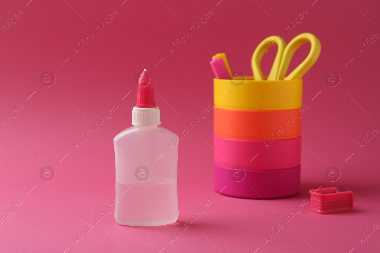 Photo of Bottle of glue, holder and scissors on pink background