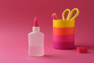 Bottle of glue, holder and scissors on pink background