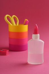 Bottle of glue, holder and scissors on pink background