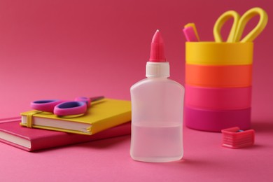 Bottle of glue, holder, scissors and notebooks on pink background