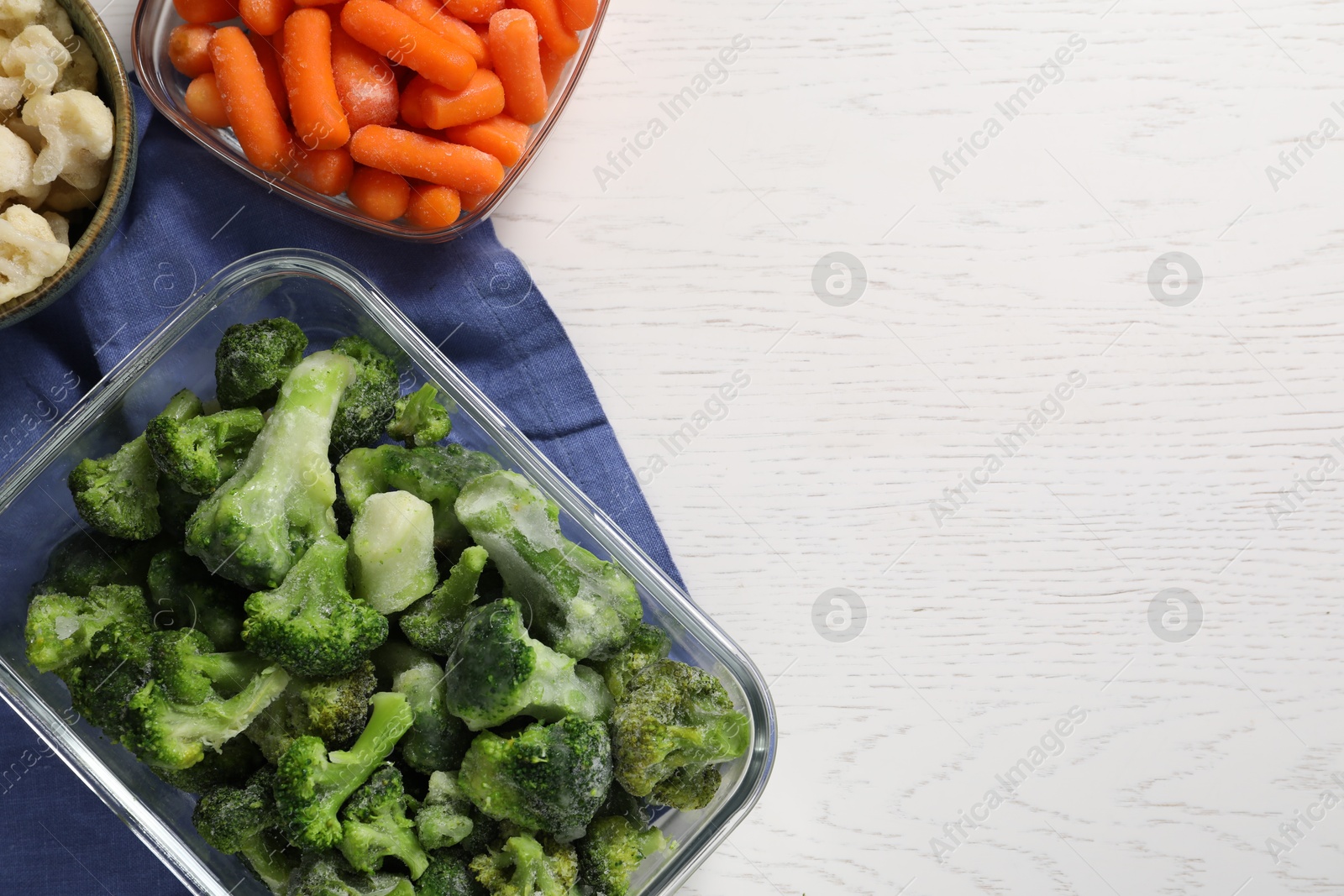 Photo of Frozen broccoli, cauliflower and baby carrots on white wooden table, top view. Space for text