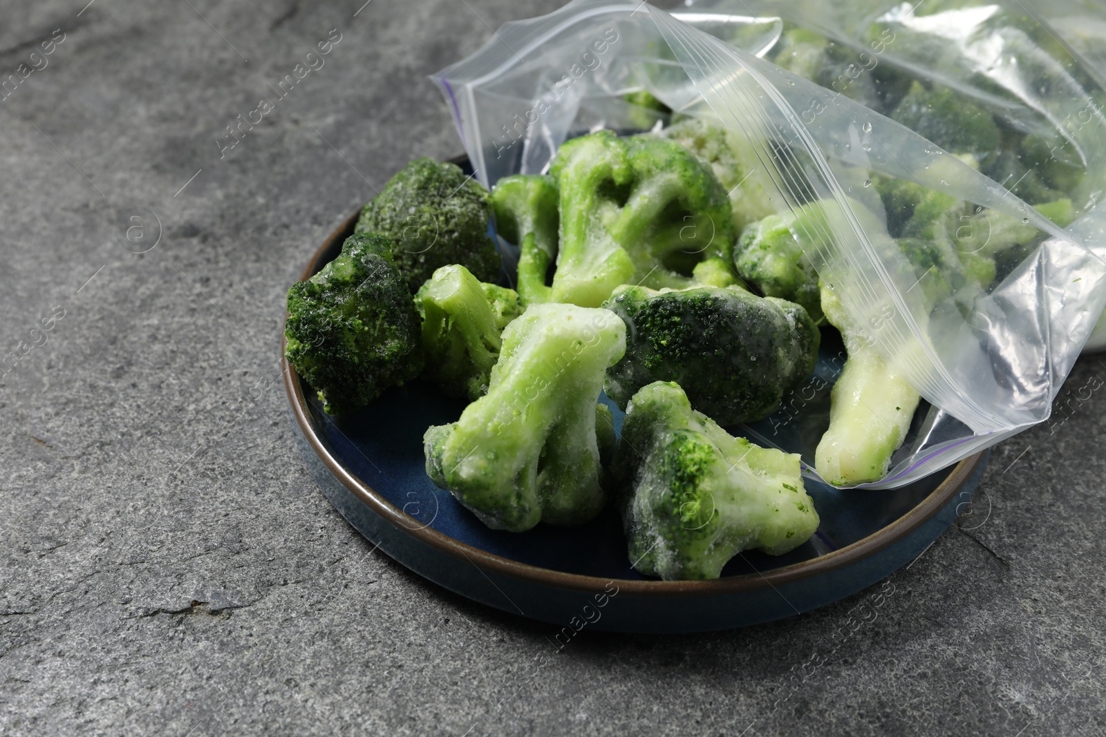 Photo of Frozen broccoli out of plastic bag on grey table, closeup