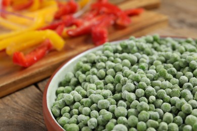 Photo of Frozen green peas in bowl on wooden table, closeup