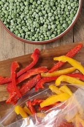 Photo of Frozen green peas in bowl and bell peppers on wooden table, top view