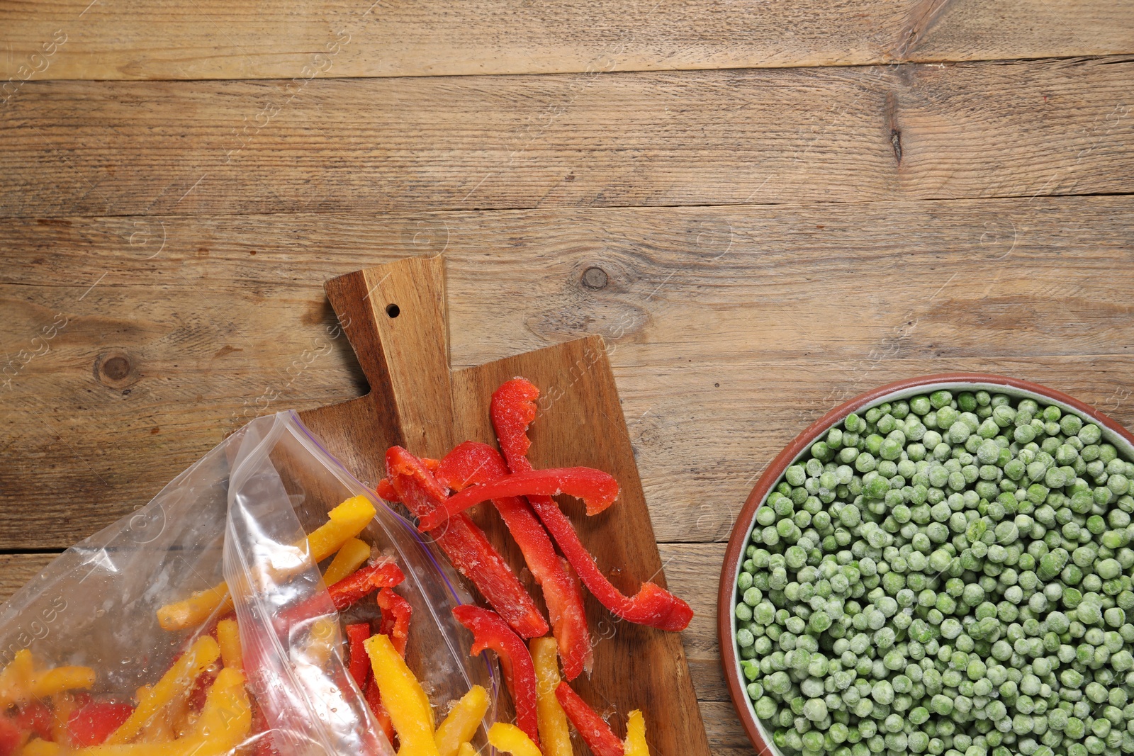 Photo of Frozen green peas in bowl and bell peppers on wooden table, top view