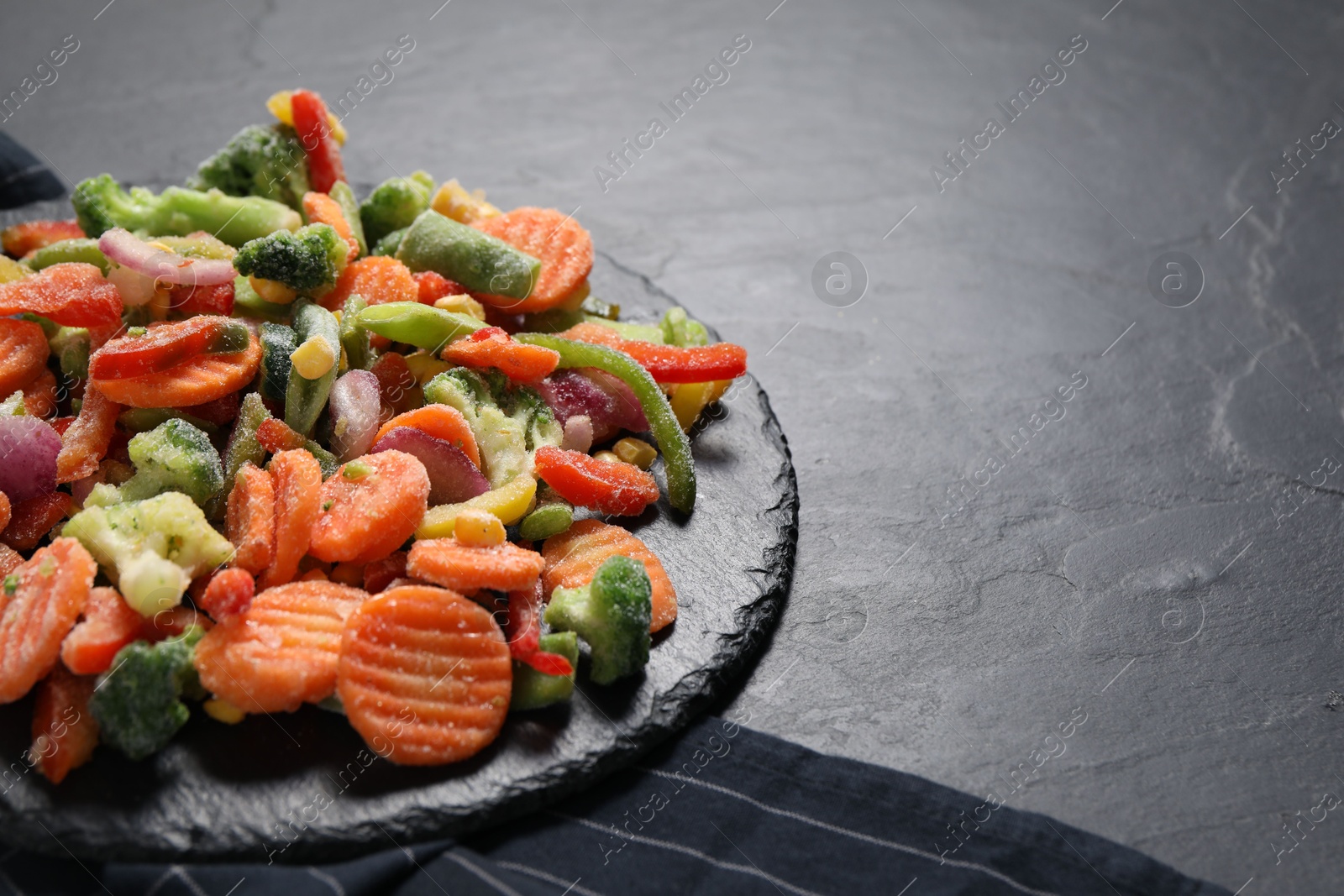 Photo of Mix of frozen vegetables on black table, closeup. Space for text