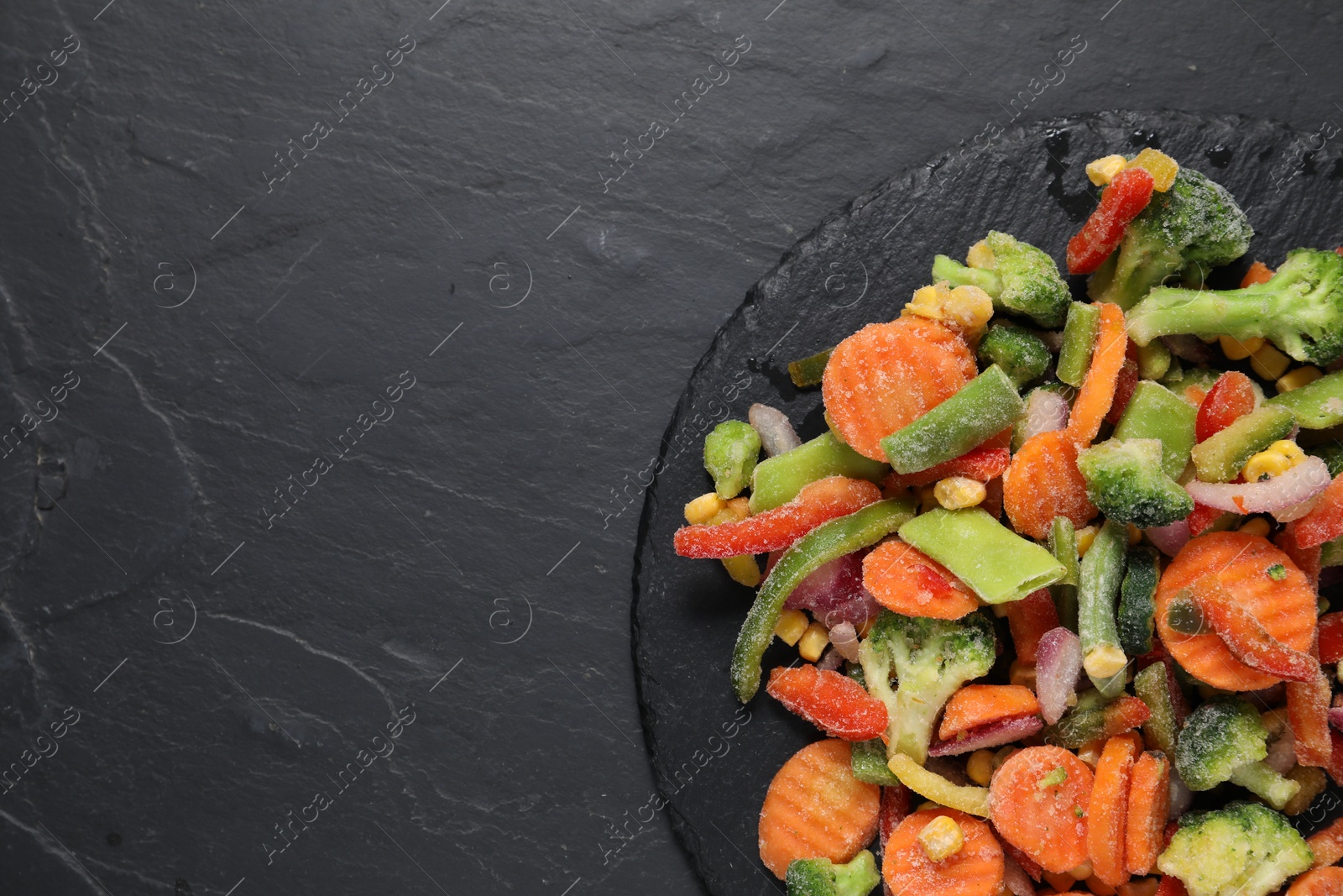 Photo of Mix of frozen vegetables on black table, top view. Space for text