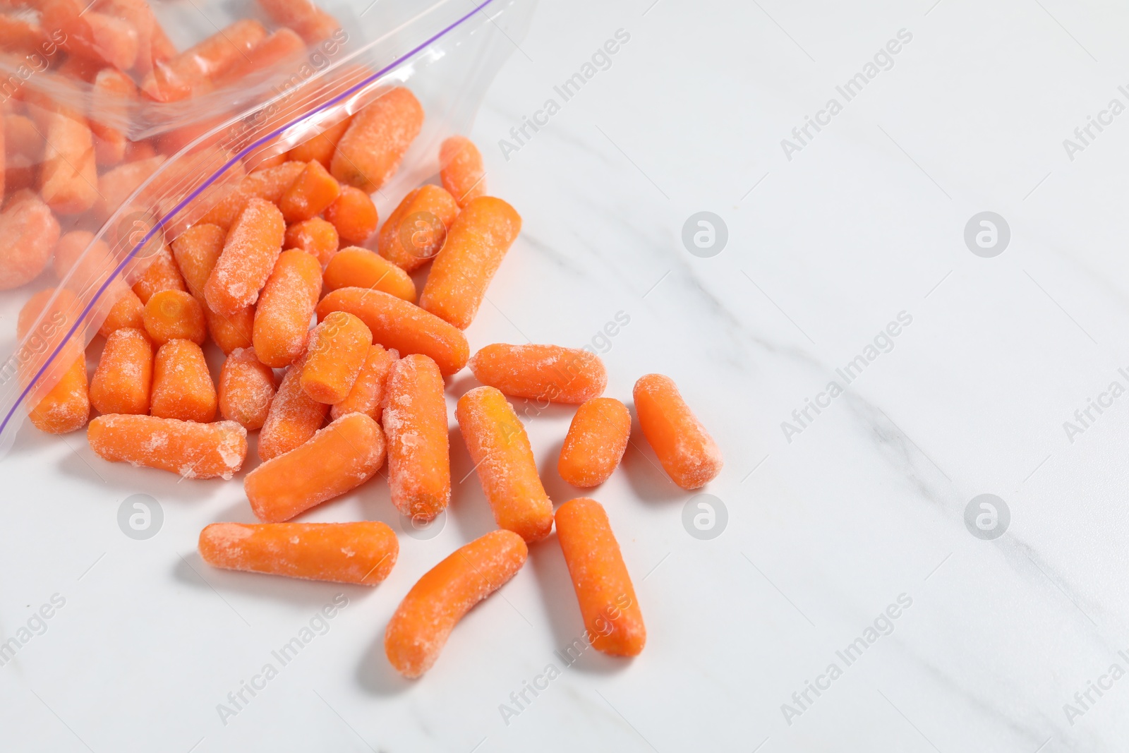 Photo of Frozen baby carrots on white marble table, closeup. Space for text