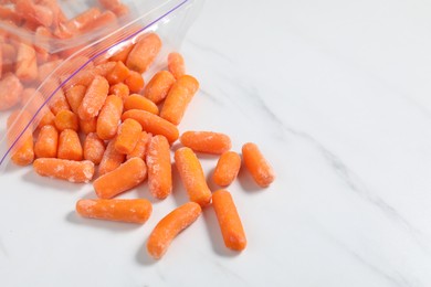 Photo of Frozen baby carrots on white marble table, closeup. Space for text