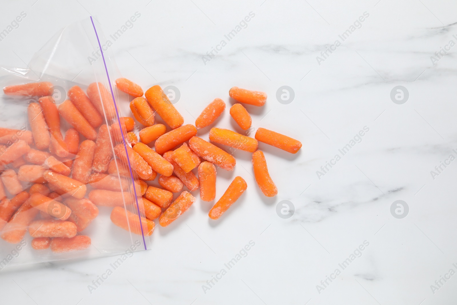 Photo of Frozen baby carrots on white marble table, top view. Space for text