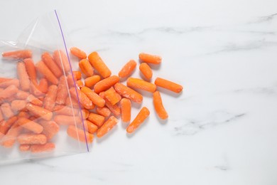 Photo of Frozen baby carrots on white marble table, top view. Space for text