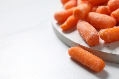 Photo of Frozen baby carrots on white table, closeup. Space for text