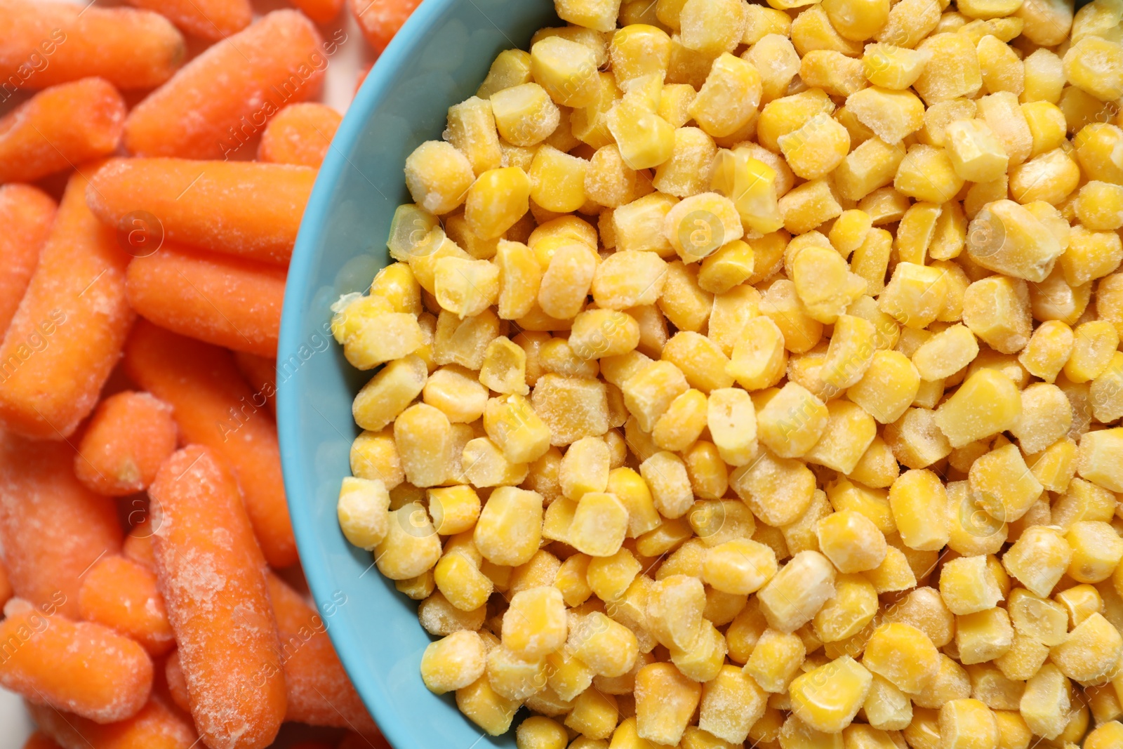 Photo of Frozen corn kernels in bowl and baby carrots on table, top view