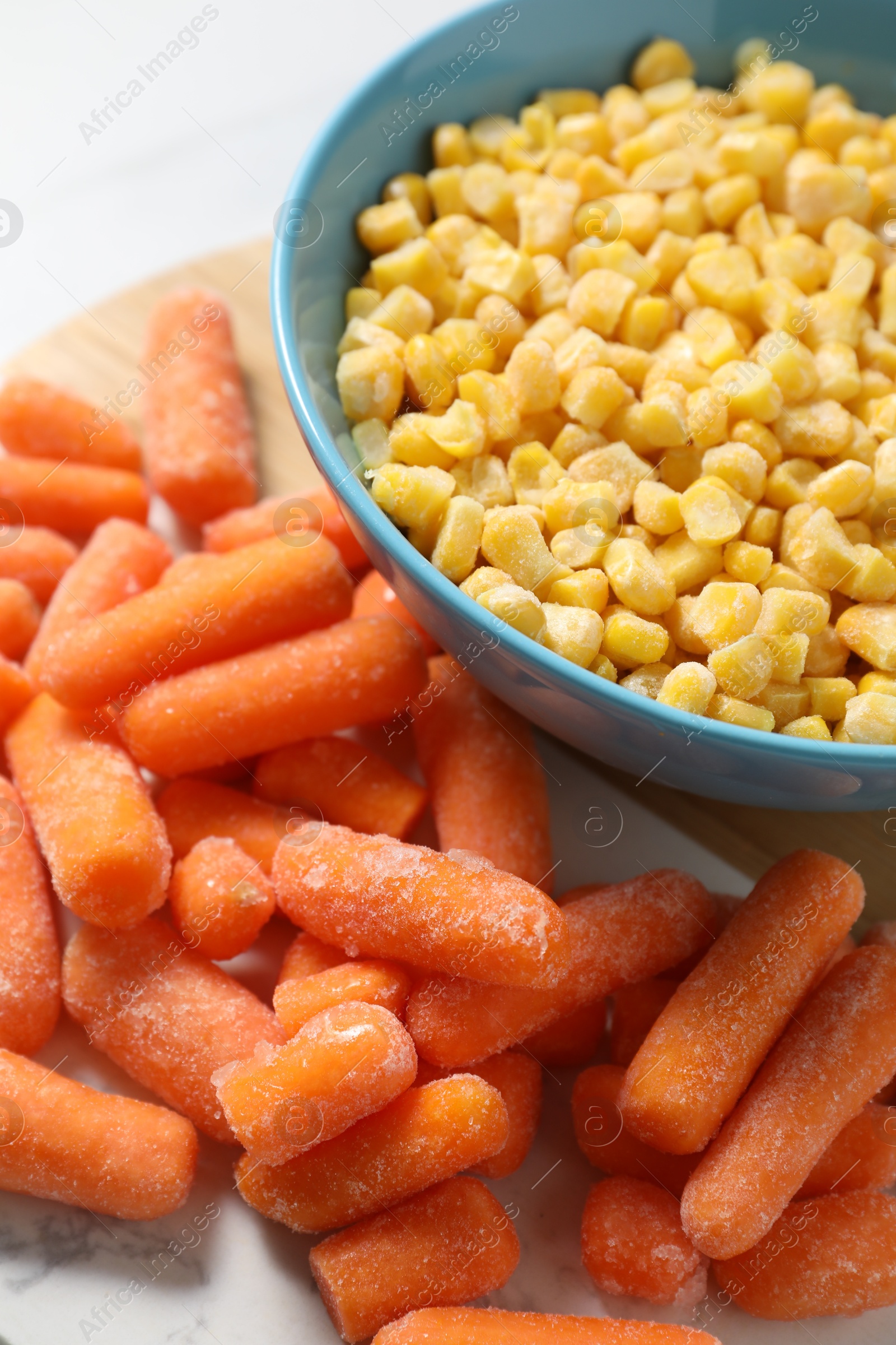 Photo of Frozen corn kernels in bowl and baby carrots on table, closeup