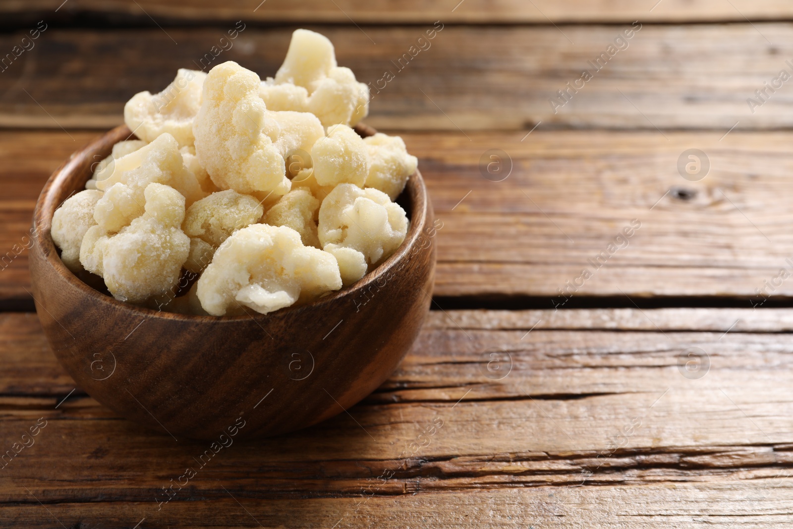 Photo of Frozen cauliflower in bowl on wooden table, closeup. Space for text