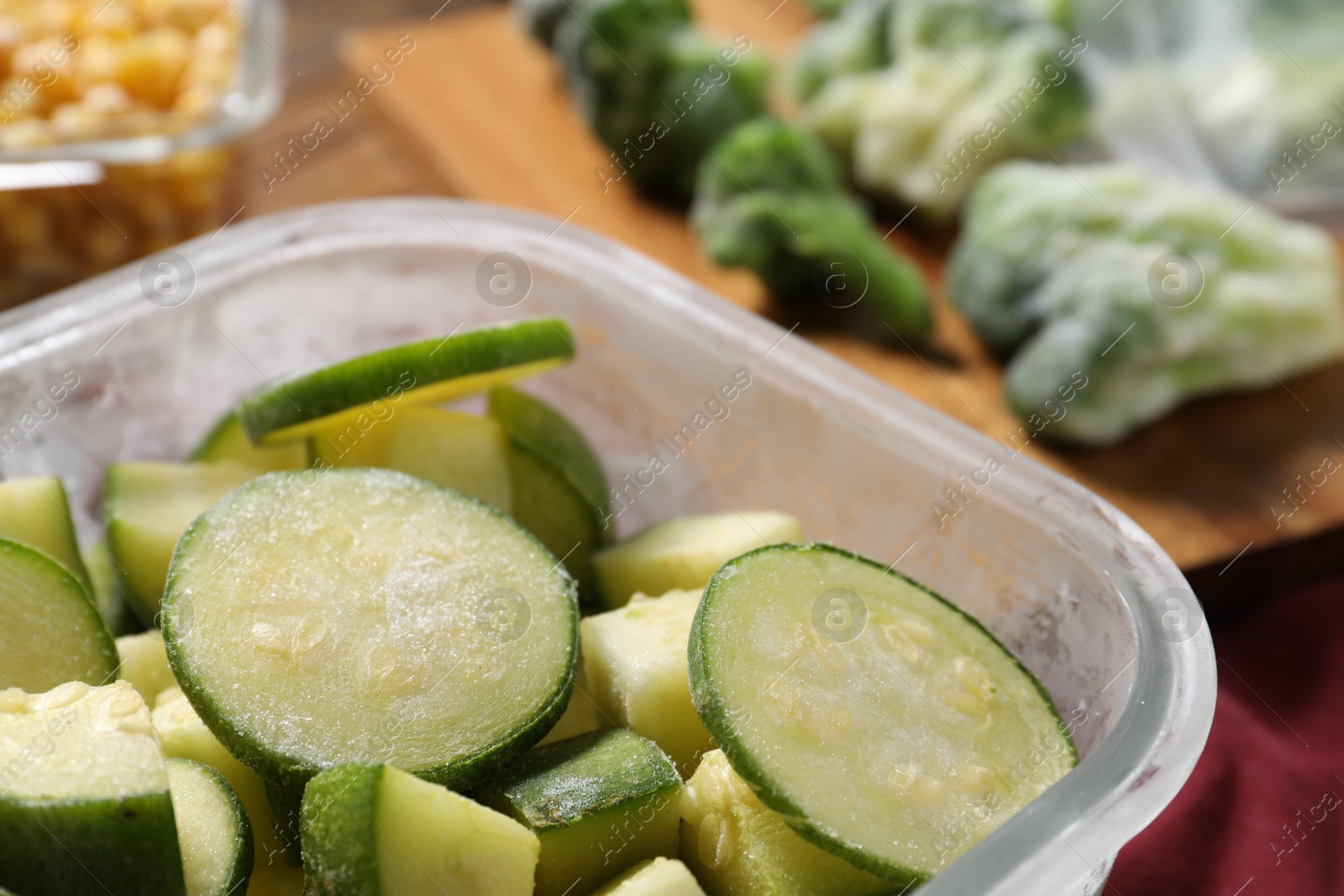 Photo of Slices of frozen zucchini in glass container on table, closeup