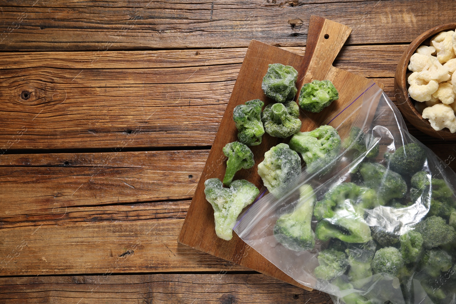 Photo of Frozen broccoli and cauliflower on wooden table, top view. Space for text