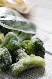 Photo of Frozen broccoli out of plastic bag on white wooden table, closeup