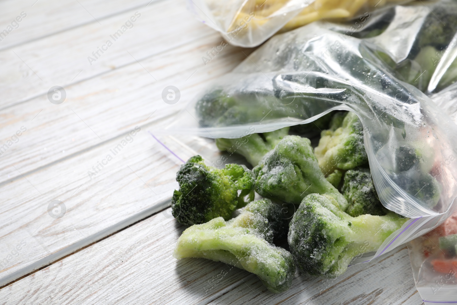 Photo of Frozen broccoli out of plastic bag on wooden table, closeup. Space for text