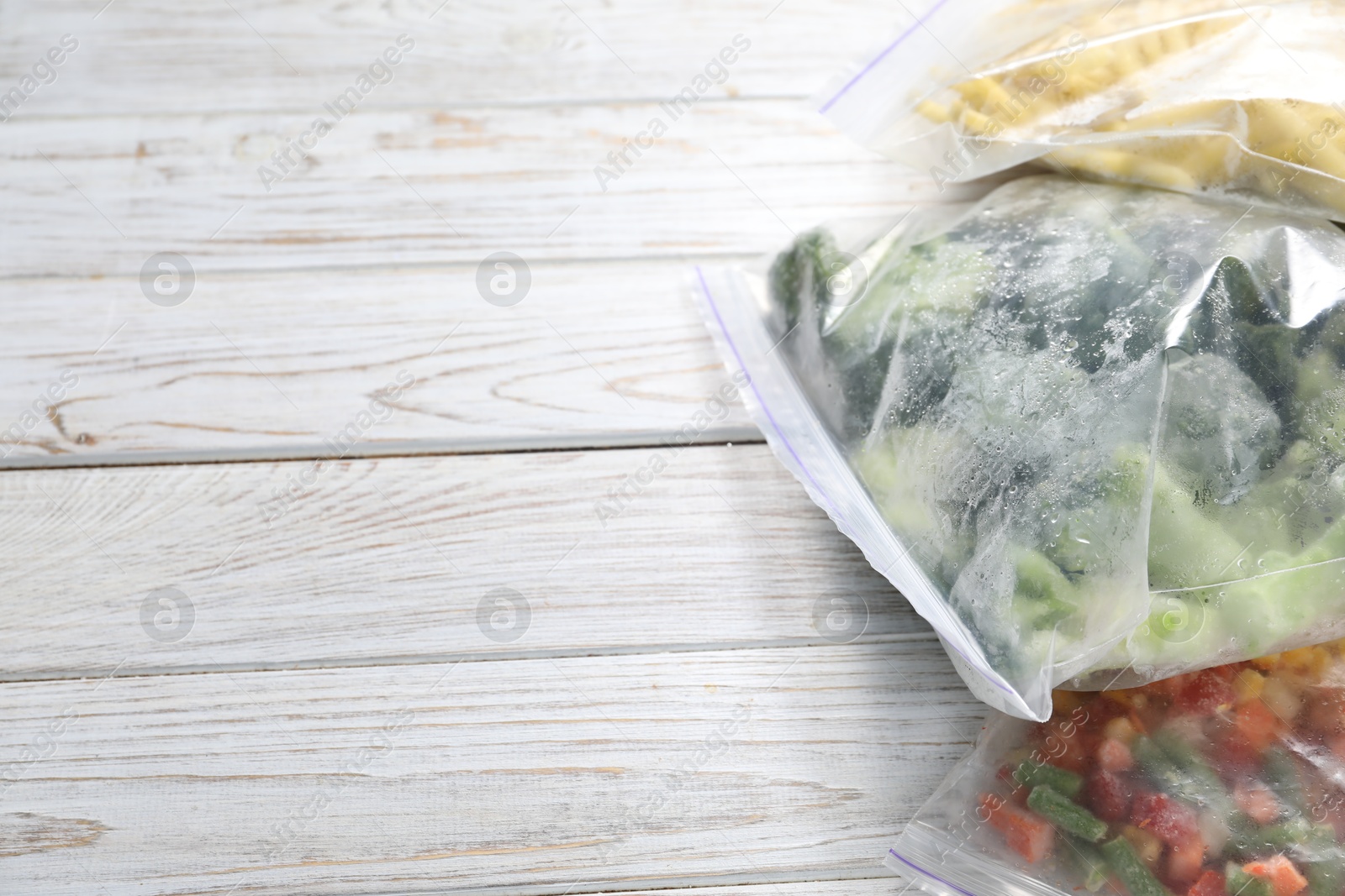 Photo of Different frozen vegetables in plastic bags on wooden table, closeup. Space for text