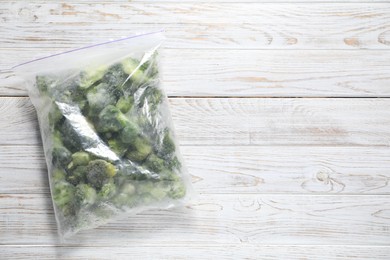 Photo of Frozen broccoli in plastic bag on wooden table, top view. Space for text