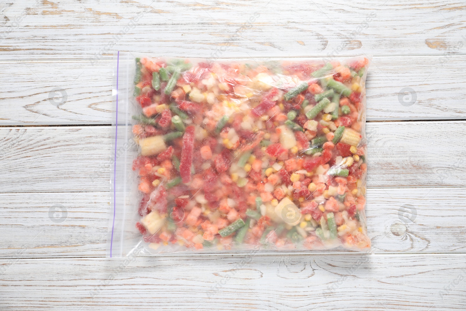 Photo of Mix of frozen vegetables in plastic bag on wooden table, top view