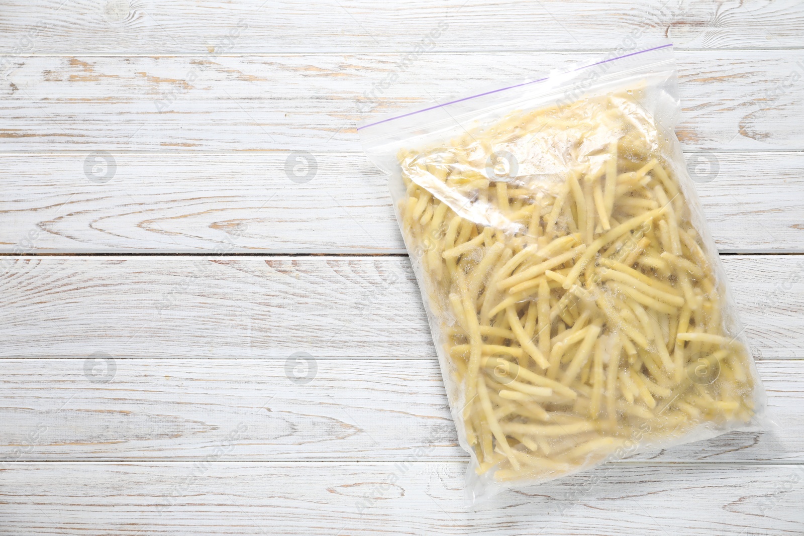 Photo of Frozen yellow beans in plastic bag on wooden table, top view. Space for text