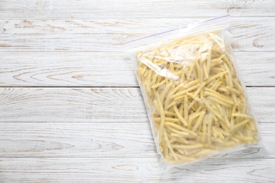 Photo of Frozen yellow beans in plastic bag on wooden table, top view. Space for text