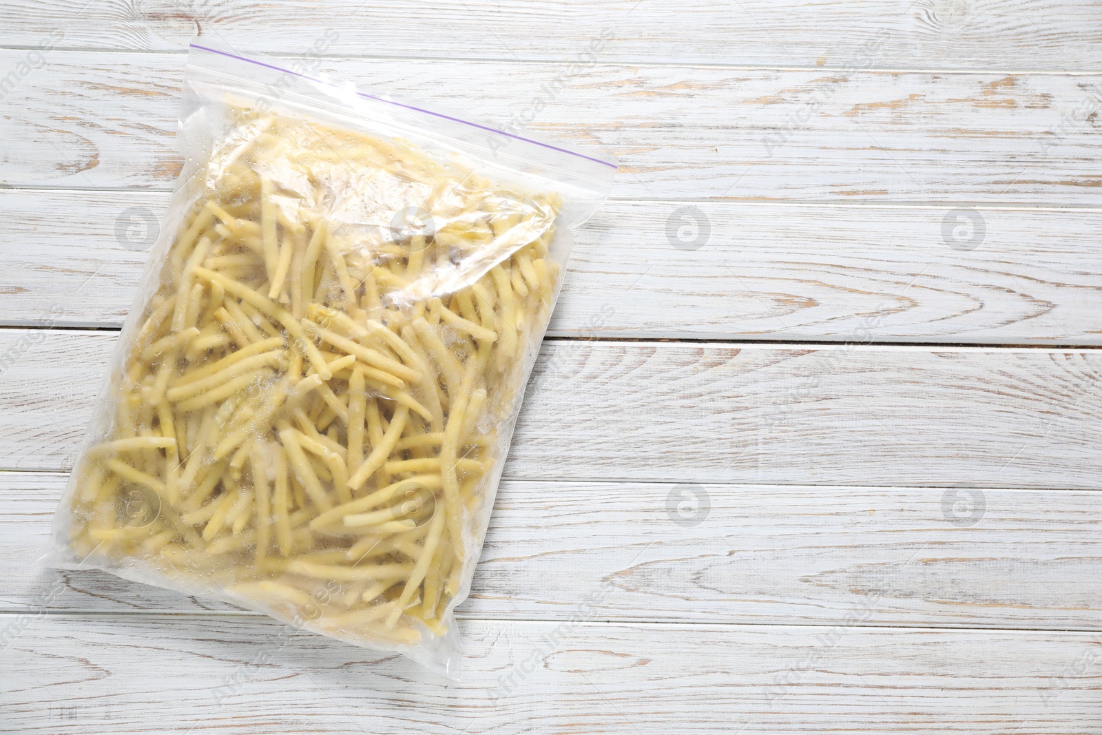 Photo of Frozen yellow beans in plastic bag on wooden table, top view. Space for text