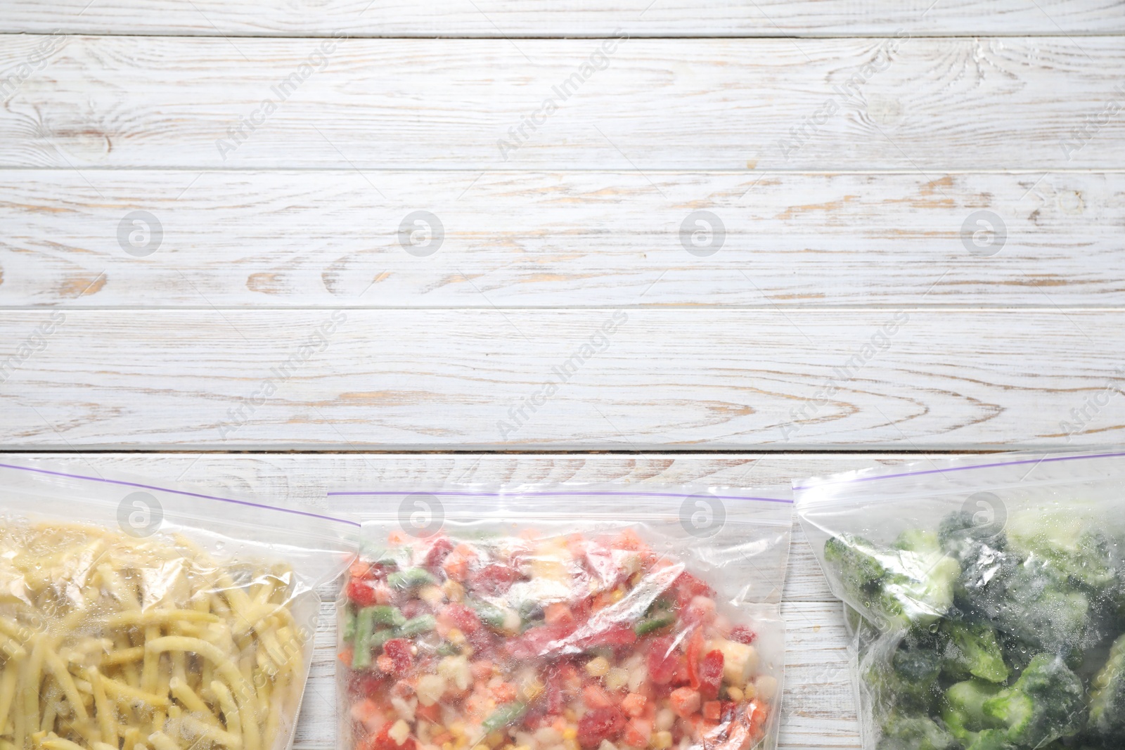 Photo of Different frozen vegetables in plastic bags on wooden table, top view. Space for text