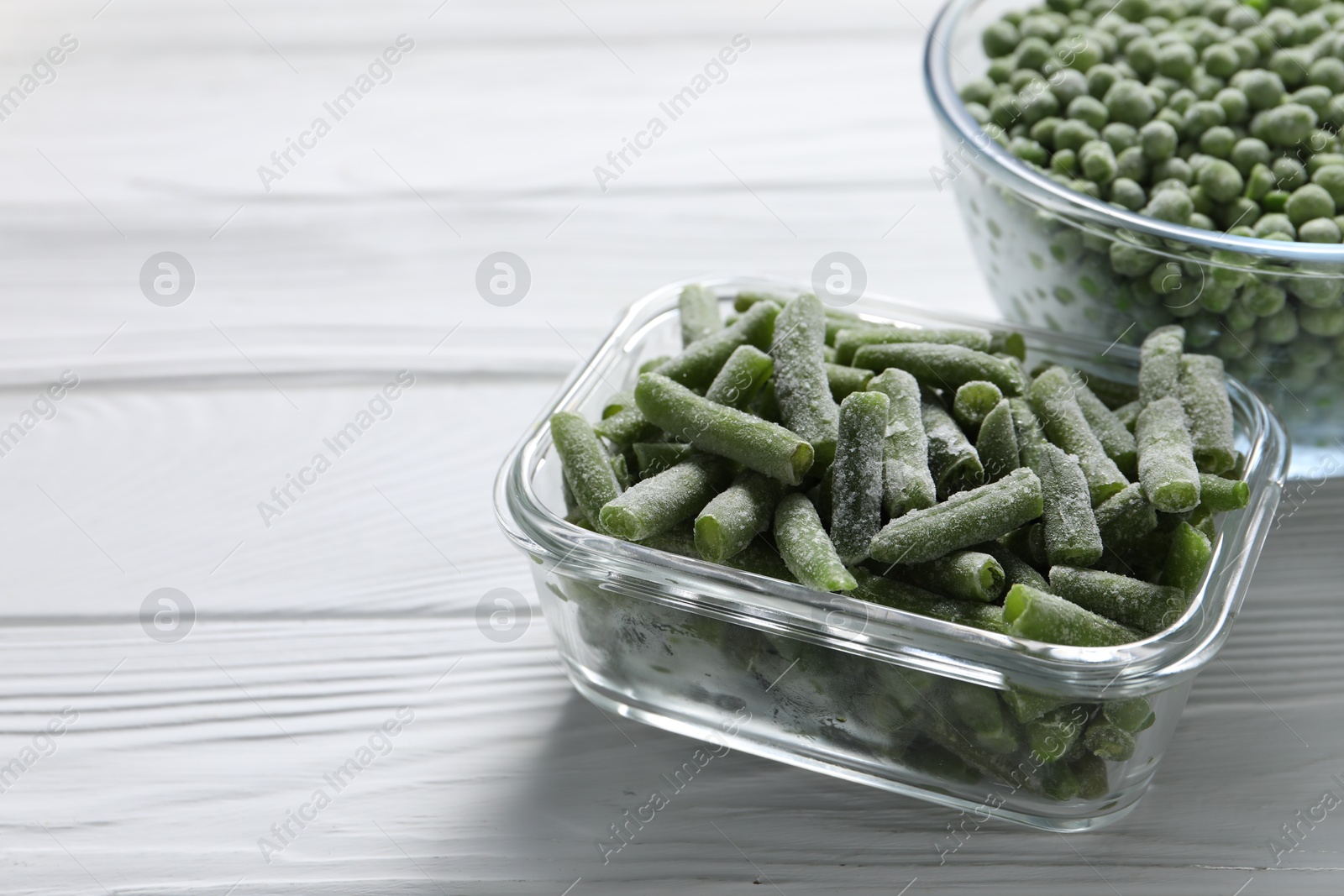 Photo of Frozen green beans and peas on white wooden table, closeup. Space for text