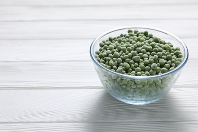 Photo of Frozen green peas in glass bowl on white wooden table, space for text