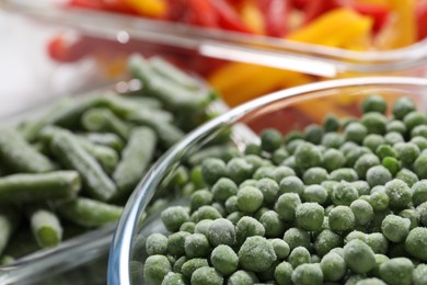 Photo of Frozen green peas in glass bowl on blurred background, closeup