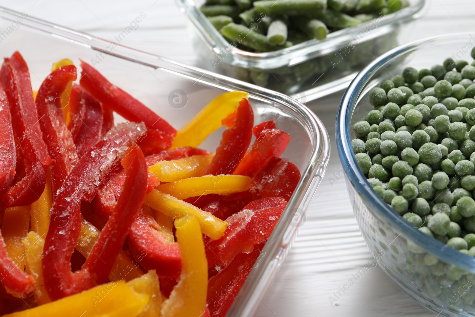 Photo of Frozen bell peppers, green peas and beans on white wooden table, closeup