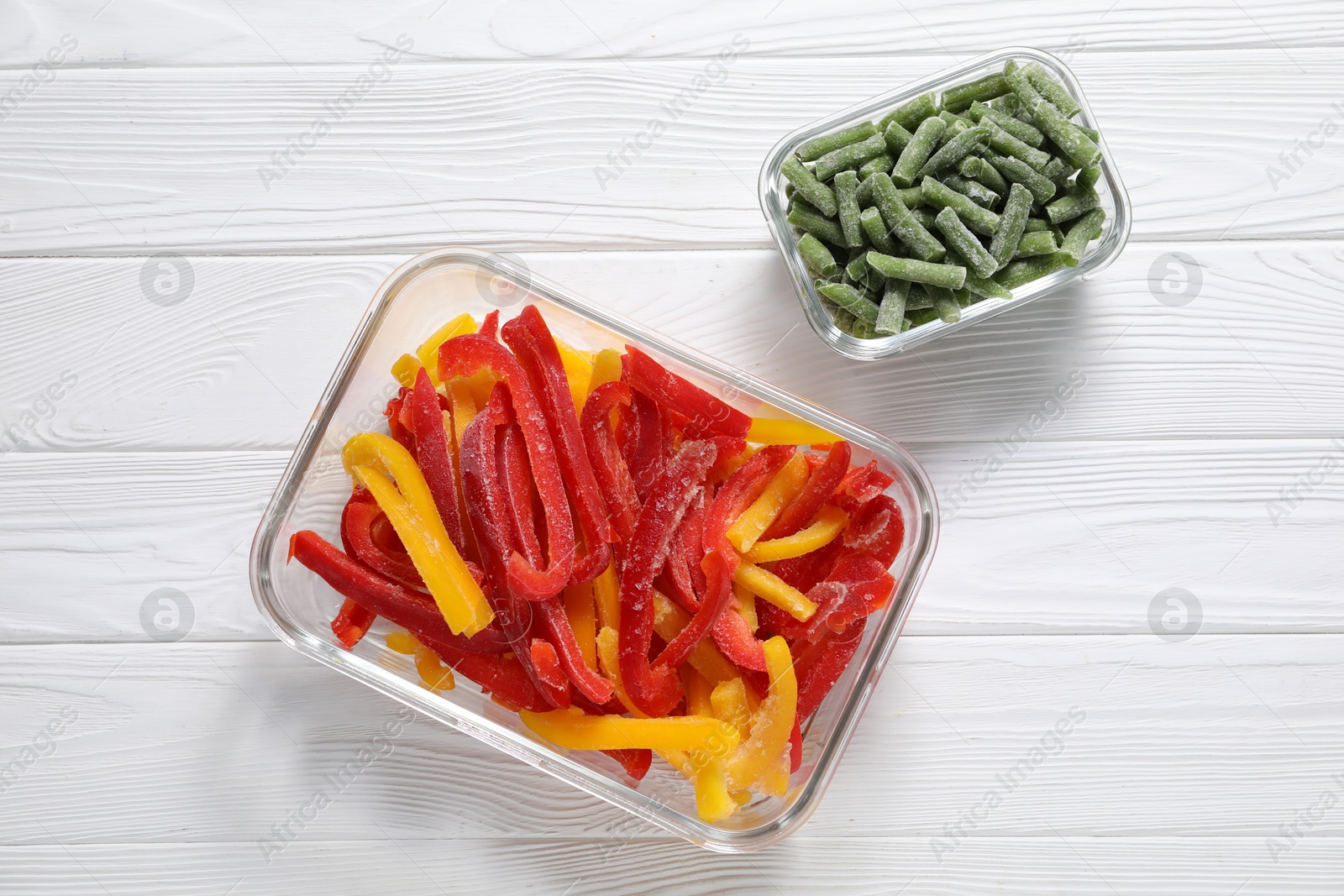 Photo of Frozen green beans and bell peppers in glass containers on white wooden table, top view