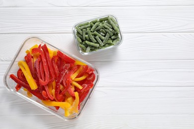 Photo of Frozen green beans and bell peppers in containers on white wooden table, top view. Space for text